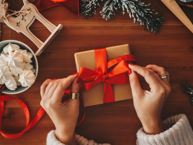 Six different christmas presents is on a table. A christmas tree is in the background.