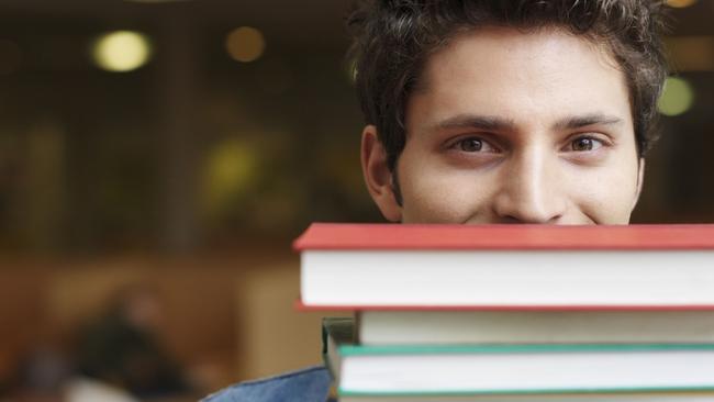 Student holding books in front of face in library, portrait