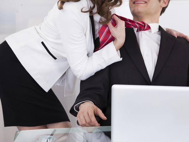 Young businesswoman pulling male colleague's tie while seducing him at desk in office