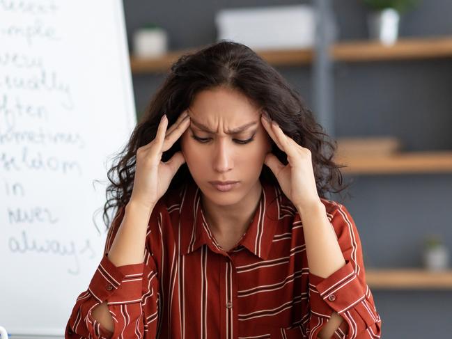 Tired From Work. Portrait of exhausted stressed young woman suffering from headache, touching and massaging her forehead and temples, sitting at desk near whiteboard, thinking about problems