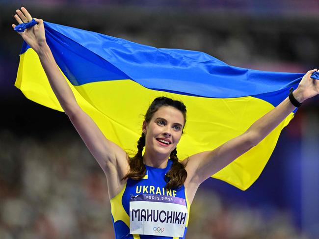 TOPSHOT - Gold medallist Ukraine's Yaroslava Mahuchikh celebrates with the Ukrainian flag after competing in the women's high jump final of the athletics event at the Paris 2024 Olympic Games at Stade de France in Saint-Denis, north of Paris, on August 4, 2024. (Photo by Martin  BERNETTI / AFP)