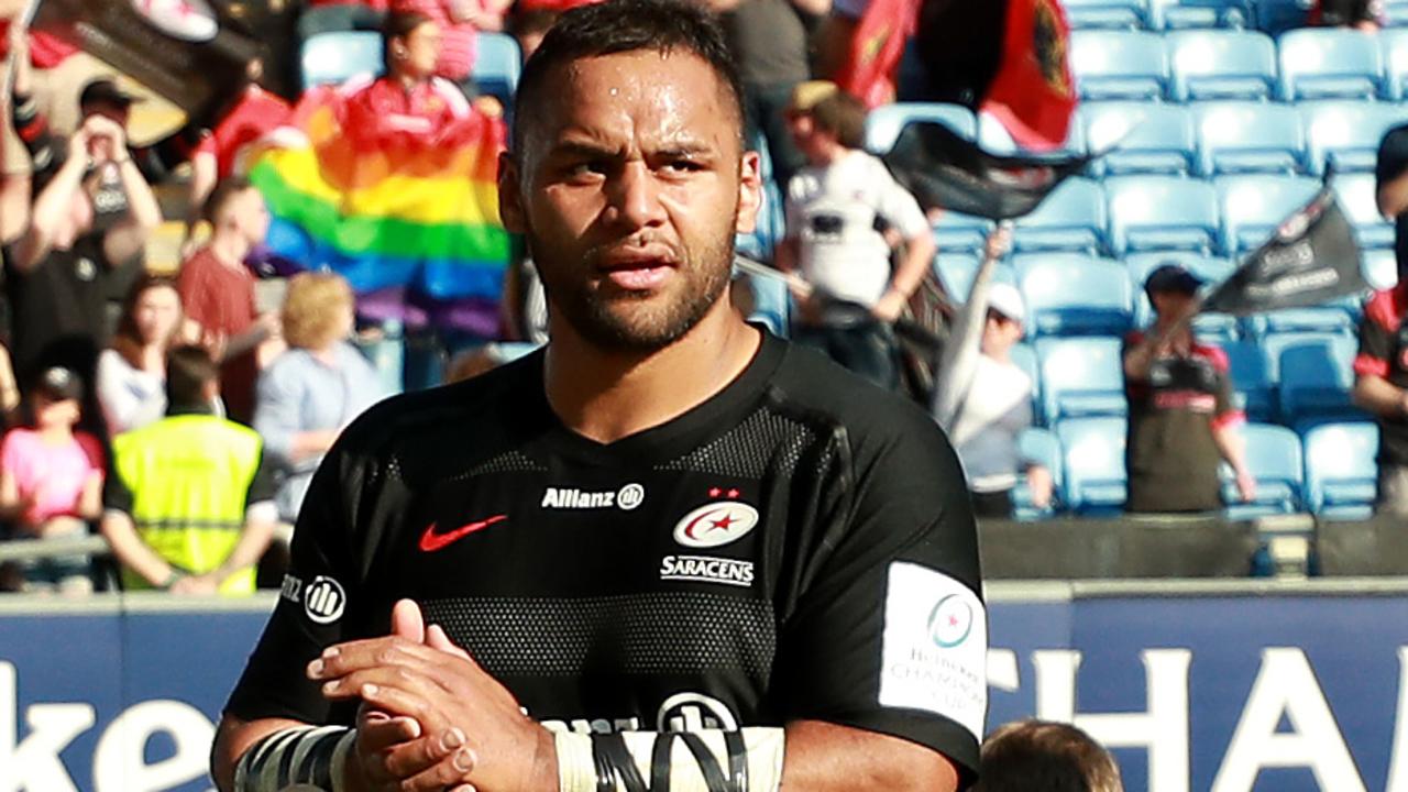 Billy Vunipola celebrates victory with a rainbow flag behind him in the stands.