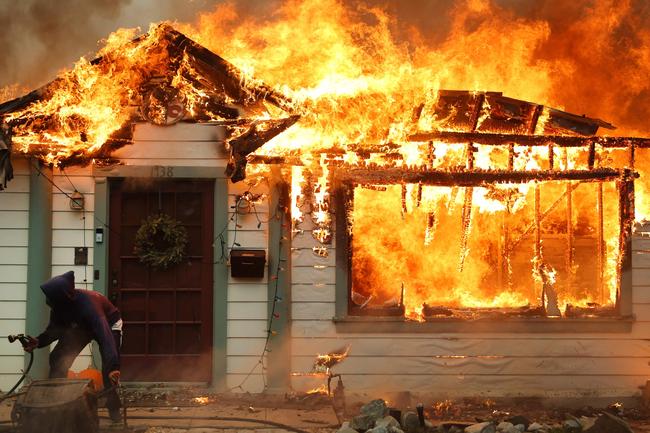 A man uses a garden hose in an effort to save a neighbouring home in Altadena. Picture: Getty Images