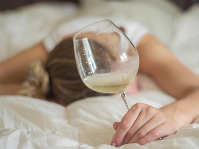 Great concept of alcohol abuse. Young woman, blond hair, fainted in bed after drinking too much alcohol. Glass of wine in hand, bottle of wine.