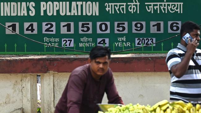 A fruits seller pushes his handcart in front of a population clock board displayed outside the International Institute for Population Sciences in Mumbai. Picture: AFP.