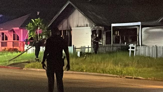 A police officer watches over the scene at a house fire in Ramsay St, Garbutt, which was under control before 9pm.