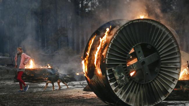 Jessica Tregellas aged 12 walks her dog past burning large NBN cable spools on the scorched property. Picture: David Caird