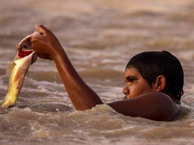 BREWARRINA, AUSTRALIA - FEBRUARY 17: A boy is seen catching a fish by hand at Brewarrina Weir on February 17, 2020 in Brewarrina, Australia. The Brewarrina Weir in Northern New South Wales overflowed on the weekend for the first time in years, as rain water from upstream flowed into the once dry river beds. The influx of water at the weir has also brought back to life the heritage listed Aboriginal fish traps, also known as Baiame's Ngunnhu. Recent rains and thunderstorms across Eastern Australia have seen a number of rivers feeding the Murray-Darling basin begin to flow. Pumping embargoes for the Barwon-Darling river system which prevent irrigators from extracting water from the river are currently in place, however there are fears that recent rainfalls may cause the NSW Government to lift the ban. (Photo by Jenny Evans/Getty Images)