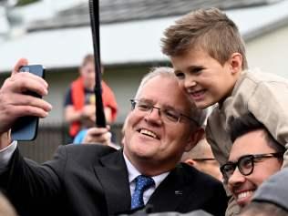 Australian Prime Minister Scott Morrison (L) takes a selfie with a local family after casting his vote outside a polling station during the Australian general election in Sydney on May 21, 2022. (Photo by SAEED KHAN / AFP)