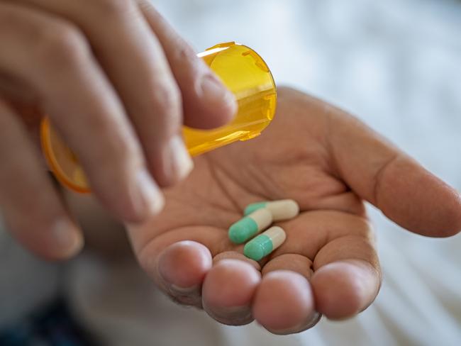 Closeup of man hand pouring capsules from a pill bottle into hand. Senior man taking daily medicine to consume. Close up of male hands taking daily dose of drug.