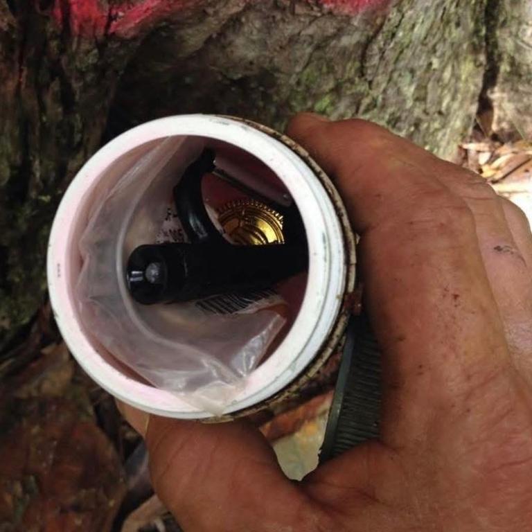 A container found beneath a tree stump that had been graffitied. It contained a torch, magnifying glass and other items.