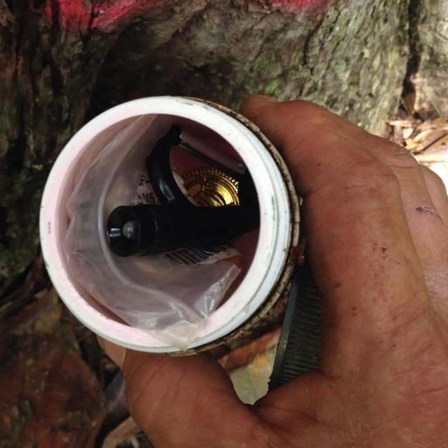 A container found beneath a tree stump that had been graffitied. It contained a torch, magnifying glass and other items.