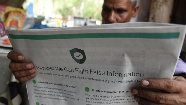 An Indian newspaper vendor reading a newspaper with a full back page advertisement from WhatsApp intended to counter fake information. Picture: AFP