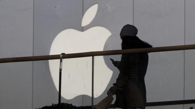 FILE - In this Dec. 23, 2013, file photo, a woman using a phone walks past Apple's logo near its retail outlet in Beijing. Even while it fiercely opposes the FBI’s demand for help unlocking an encrypted iPhone used in the San Bernardino mass shootings, Apple has never argued that it isn’t capable of doing what the government wants. While the FBI may have found an alternative solution in the San Bernardino case, experts say it’s almost certain that Apple and other tech companies will keep increasing the security of their products, making it harder or perhaps even impossible for them to answer government demands for customers’ data. (AP Photo/Ng Han Guan, File)