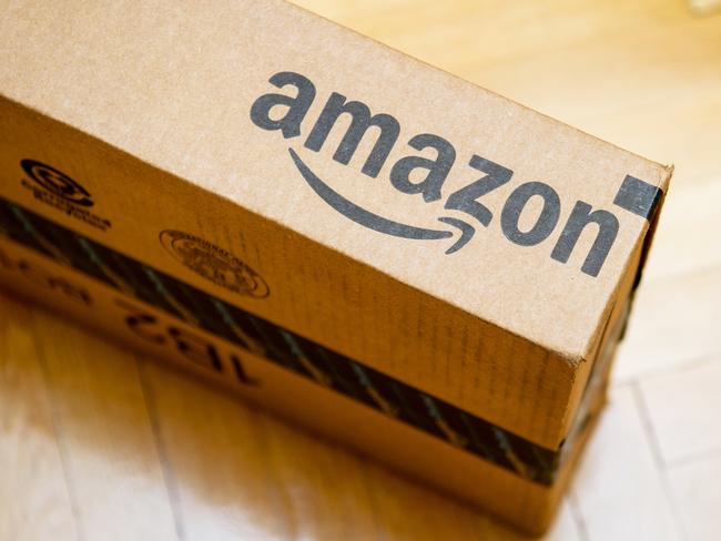 Amazon logotype printed on cardboard box side seen from above on a wooden parquet floor. Amazon is an American electronic e-commerce company distribution worlwide e-commerce goods