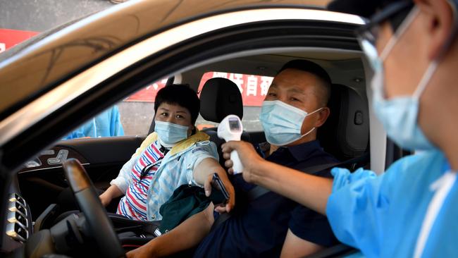 A security personnel wearing a protective suit checks the temperature of people entering the Xinfadi market in Beijing on Sunday after a new cluster linked to the market. Picture: Noel Celis/ AFP.