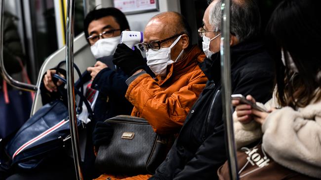 A man checks his body temperature with a non-contact infrared thermometer while commuting on a train in Tokyo. Picture: AFP