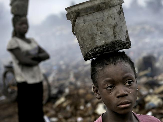 Fati, eight, cries as she searches through hazardous waste for scrap metal, because of the pain of her malaria. Picture: Renee Byer