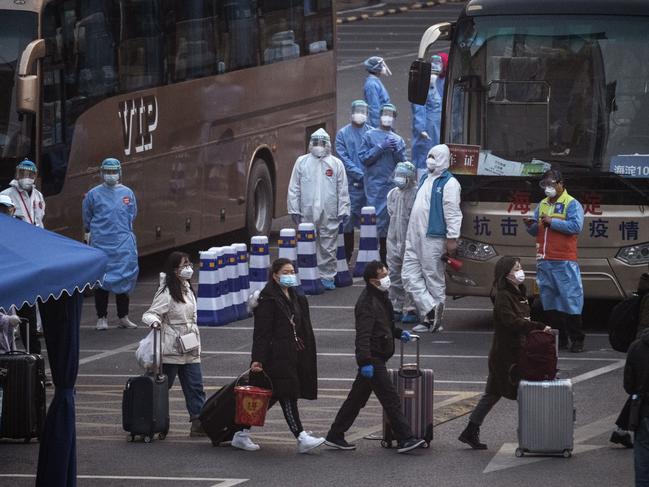 Chinese workers and health officials wear protective suits as they watch travellers from Hubei province, including Wuhan, as they gather to take buses. Picture: Getty