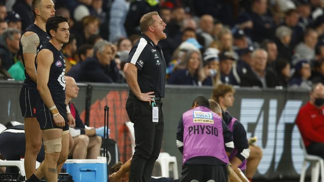 Michael Voss coaches Carlton from the bench as physios work on a player.