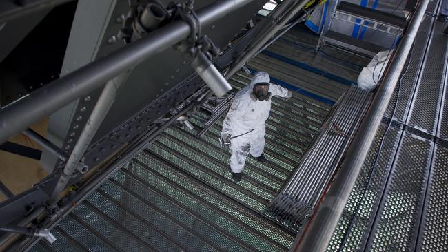 Matt Flemming stands on a metal grill above the harbour as he prepares to spray paint. Photos: Chris McKeen