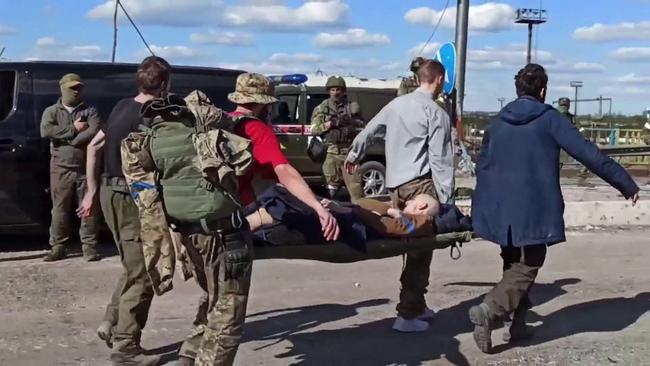 A Ukrainian service member carried on a stretcher escorted by pro-Russian military personnel after leaving the besieged Azovstal steel plant. Picture: AFP
