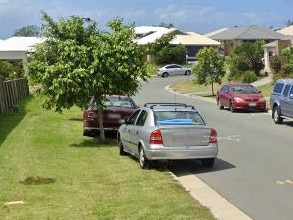 Cars parked with two wheels on the grass on a road in Coomera.