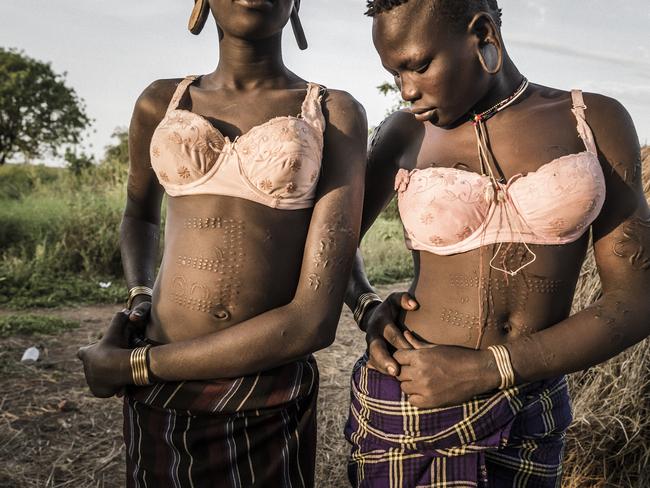 Ethiopia. Mago National Park. 2017. Two girls from the Mursi ethnic group are getting ready to return to their village, after going to get some water in a well. Both wear bras that have been given to them by western tourists. Picture: Fausto Podavini/World Press Photo