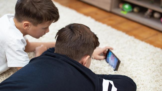 R44YH4 Little boys watching video by smartphone on carpet at home, rear view