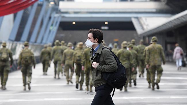 A man wearing a face mask walks past members of the Australian Defence Force at Spencer St station. Picture: Getty