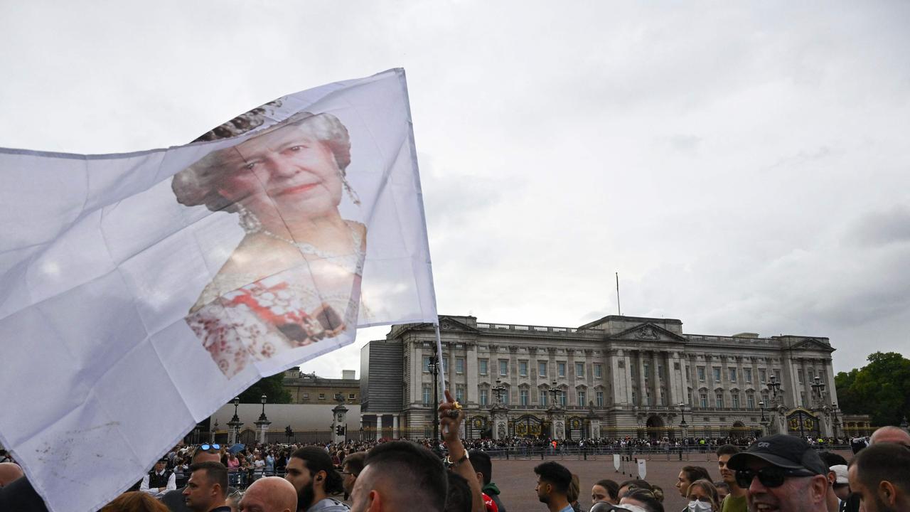 A mourner waves a flag with the face of Britain's Queen Elizabeth II on outside of Buckingham Palace in London. Picture: Sebastien Bozon / AFP