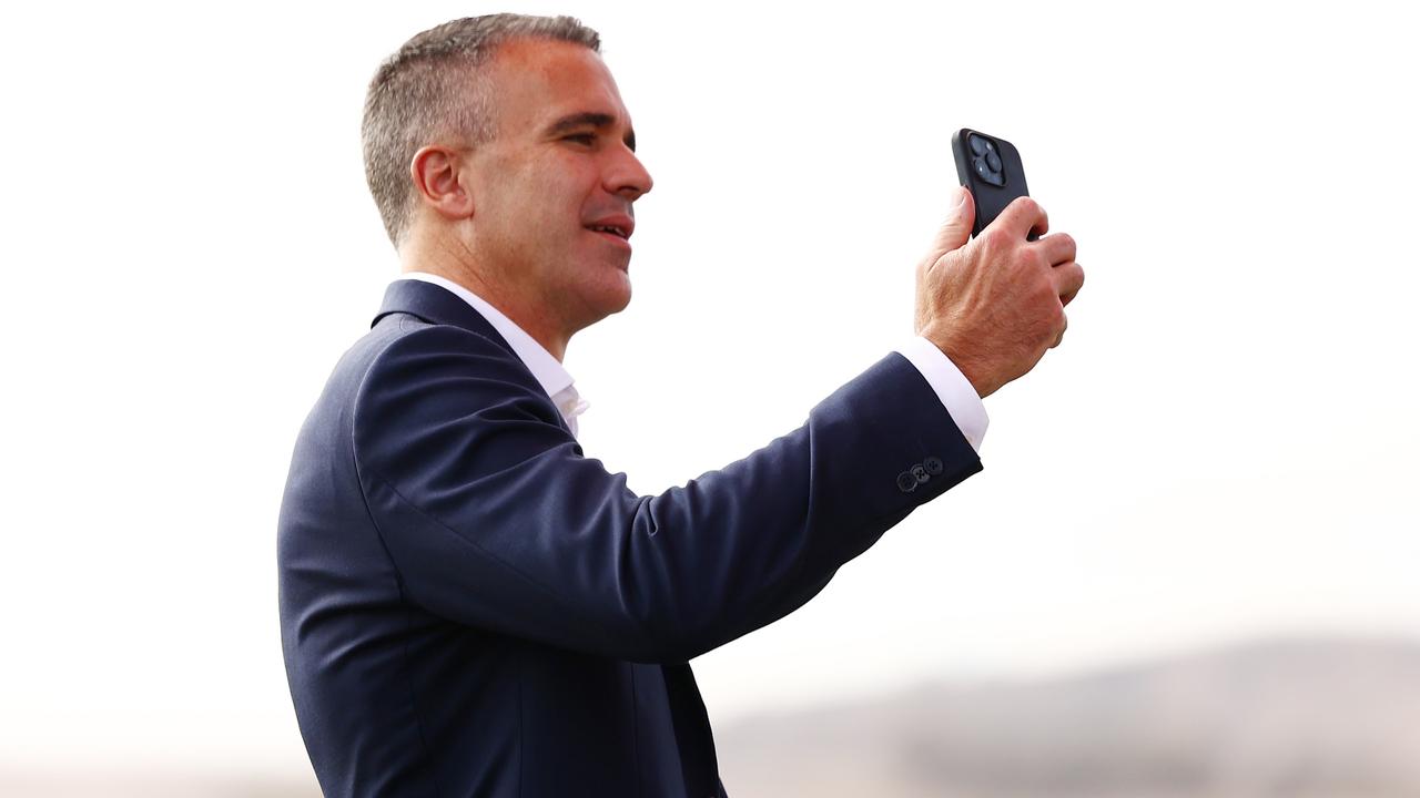 Premier Peter Malinauskas takes photos on his phone during an April 10 media call ahead of the first AFL game at Barossa Park for Gather Round. (Photo by Morgan Hancock/AFL Photos/via Getty Images)