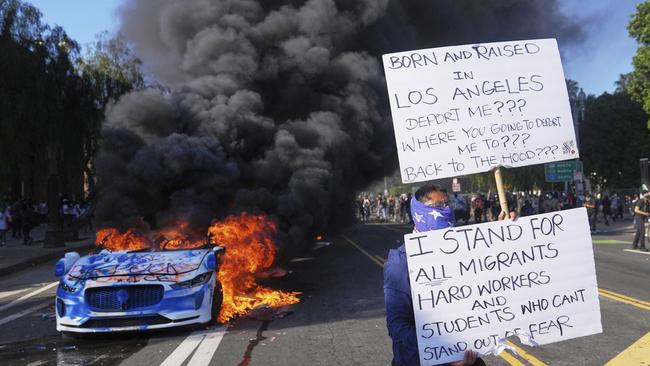 A protester is seen as a Waymo taxi burns near the federal Metropolitan Detention Centre in downtown Los Angeles on Sunday local time. AP Photo/Jae C. Hong