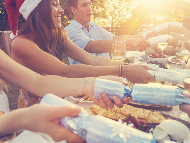 Group of people pulling Christmas crackers. There is food on the table outdoors in a December Summer. There is Cheese and wine. low angle view. Some people are wearing Santa hats