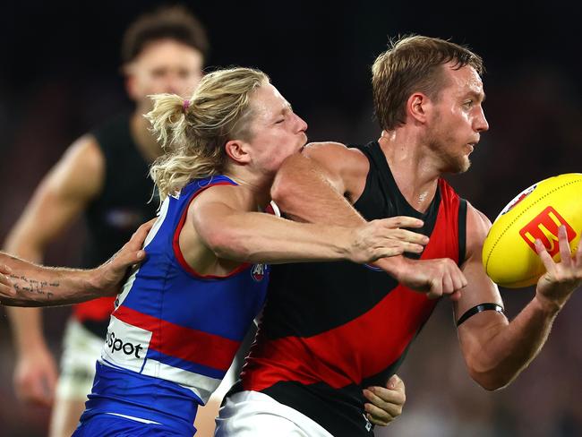 MELBOURNE, AUSTRALIA – APRIL 12: Darcy Parish of the Bombers handballs while being tackled by Cody Weightman of the Bulldogs during the round five AFL match between Western Bulldogs and Essendon Bombers at Marvel Stadium, on April 12, 2024, in Melbourne, Australia. (Photo by Quinn Rooney/Getty Images)