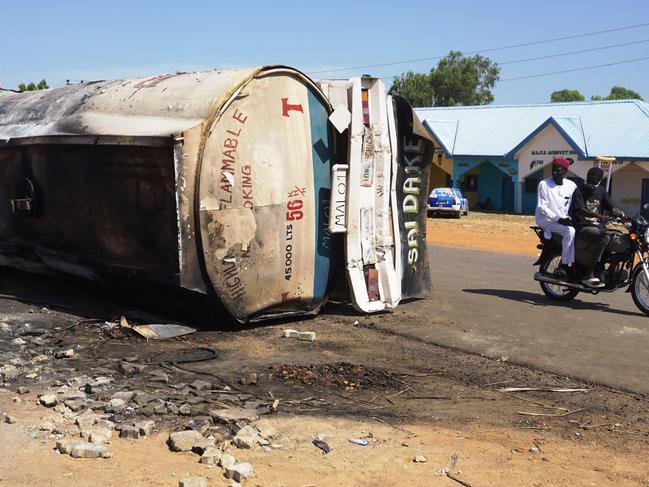 TOPSHOT - A motorcycle rides past the remain of a fuel tanker whose explosion killed almost 150 people in. An explosion tore through crowds of people who had rushed to collect fuel spilling from a crashed tanker in northern Nigeria, killing at least 147, officials told AFP on Wednesday. The tragedy is the latest such accident at a time when petrol has become a precious commodity in the country, which is suffering its worst economic crisis in a generation. The fuel tanker veered to avoid another vehicle and crashed in the town of Majiya, Jigawa state late on Tuesday, police said. (Photo by Aminu ABUBAKAR / AFP)