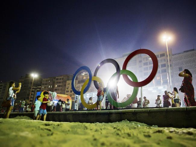 People pose for photos in front of the Olympic rings along Copacabana beach