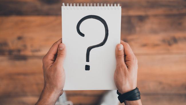 Top view of man holding note pad with question mark on it while standing on the wooden floor