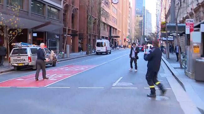 A firey with a fireman’s axe and a civilian with a chair approach Ney as he waves the knife around while backing down the street. Picture: Seven News