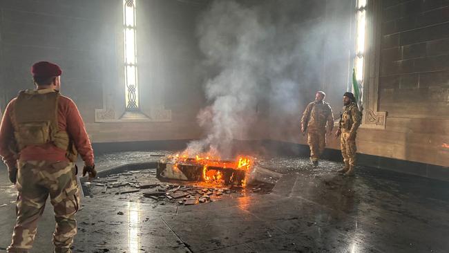 Rebel fighters stand next to the burning gravesite of Syria's late president Hafez al-Assad at his mausoleum in the family's ancestral village of Qardaha. Picture: AFP