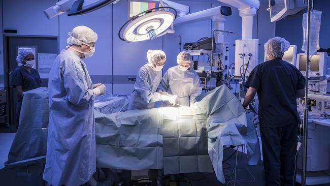 Four doctors in hospital operating room with patient lying on operating table. Surgical lights shining on medical team performing operation on patient – Picture iStock