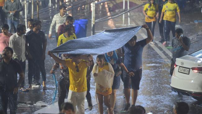 Cricket fans take refuge under a plastic sheet during heavy rains as they leave the IPL final.