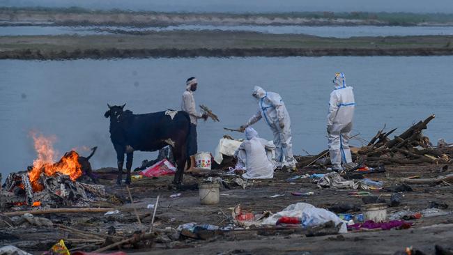 Relatives in personal protective equipment suits perform the last rites before the cremation of their loved one on the banks of the Ganges River in India. Picture: AFP