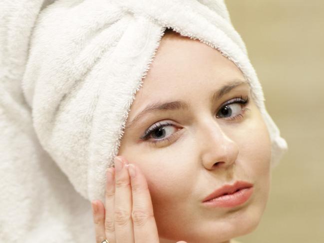 Portrait of a young attractive woman applying moisturizer in a bathroom.