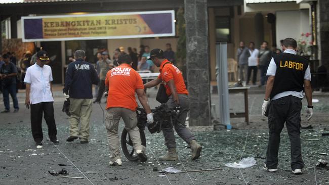 Officers remove the wreckage of a motorcycle from the site of an attack outside a church in Surabaya. Picture: AP.