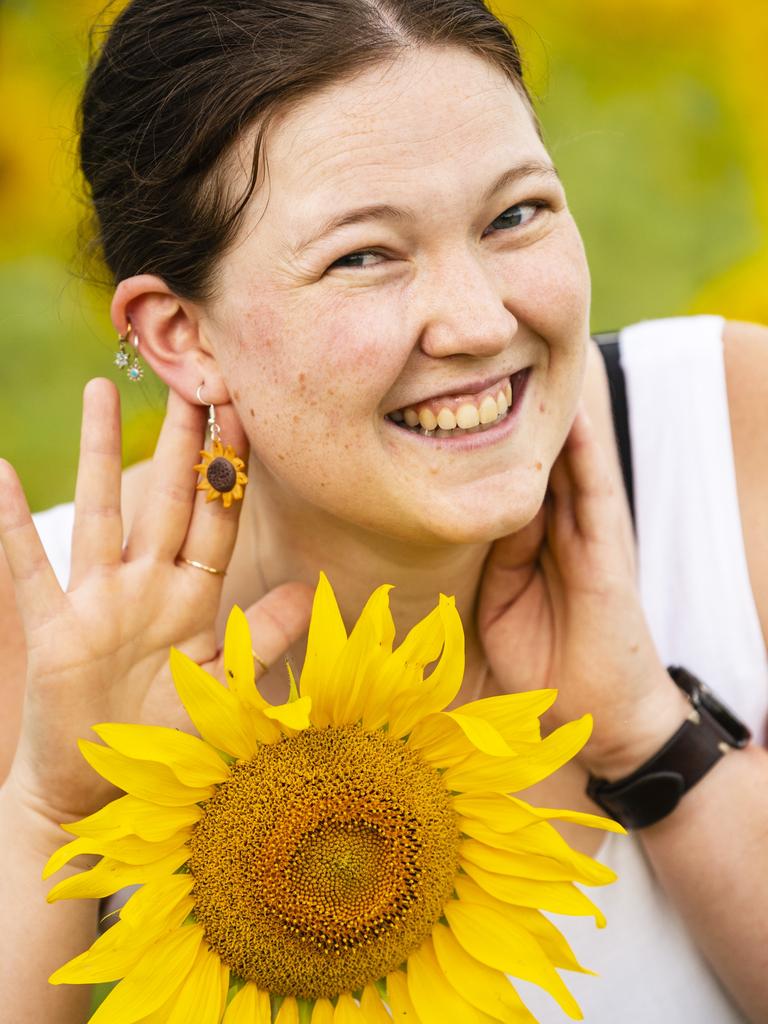 Laura Hoek shows off her sunflower earrings while standing in the Warraba Sunflowers summer crop, Wednesday, January 4, 2023.