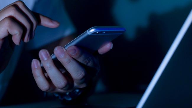 close up young man hand holding smartphone for access by unlock on screen and using laptop for register website on internet in the late night , internet addiction concept