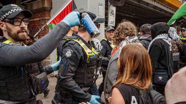 MELBOURNE, AUSTRALIA. NewsWire Photos. SEPTEMBER 8, 2024. A police officer prepares to deploy pepper spray as demonstrators wave Palestinian flags during a protest in Melbourne. Tensions rose between protesters and police under the bridge near Flinders Street Station. Picture: NewsWire/Tamati Smith.