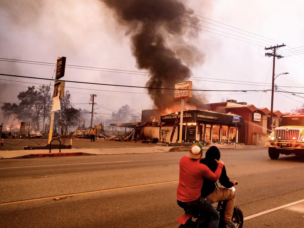 AFTER: Residents ride their motorbike past a burning liquor store during the Eaton fire in the Altadena area of Los Angeles County. Picture: AFP via Getty Images