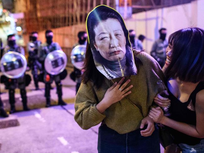 A woman wears a face mask depicting Secretary for Justice Teresa Cheng as she poses in front of a line of riot police in Hong Kong. Picture: AFP